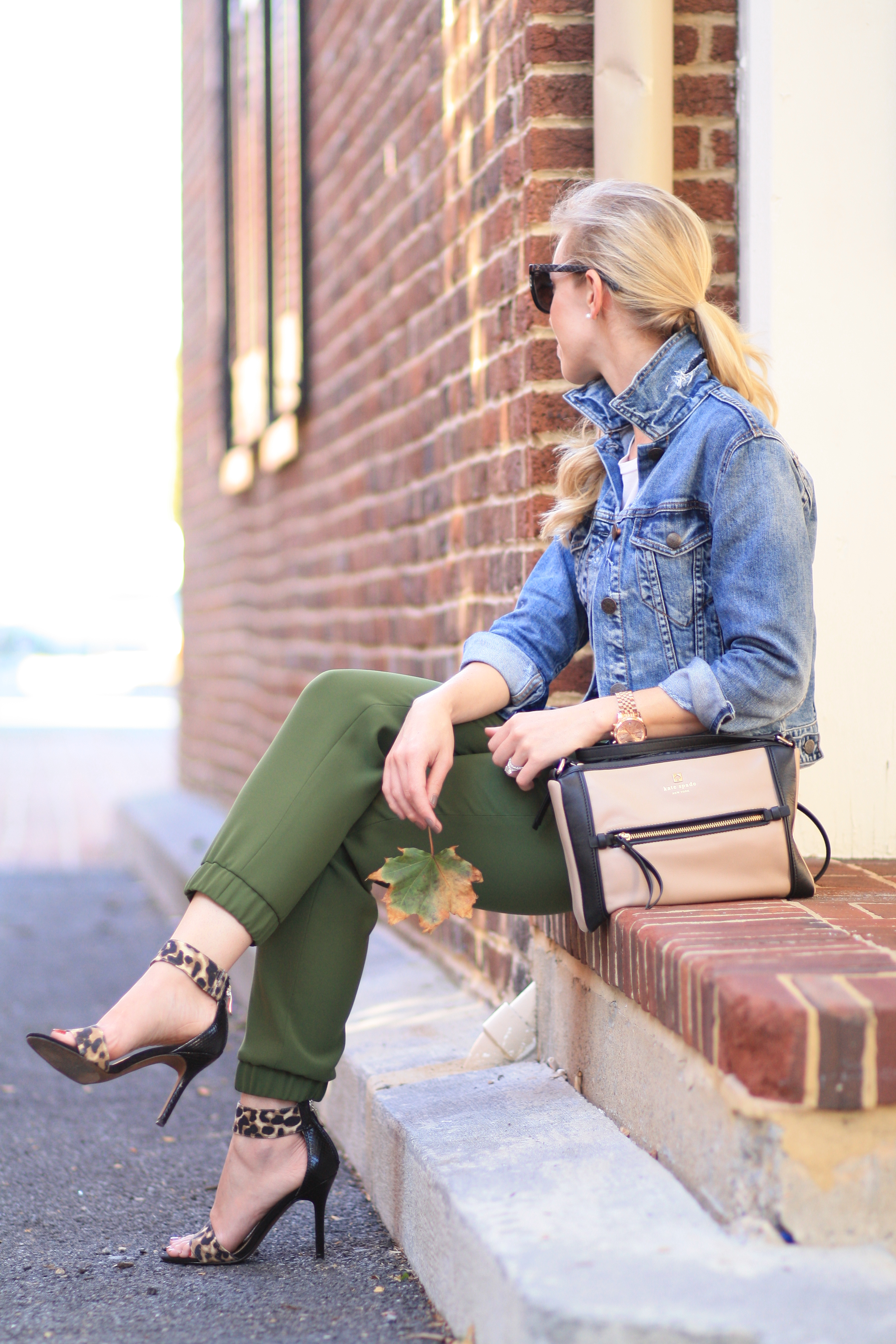 J. Crew distressed denim cropped jacket, cuffed sleeves, popped collar on  denim jacket, olive track pants, tapered track pants, leopard ankle strap  heels, Kate Spade colorblock bag, black Chanel cateye sunglasses, fall