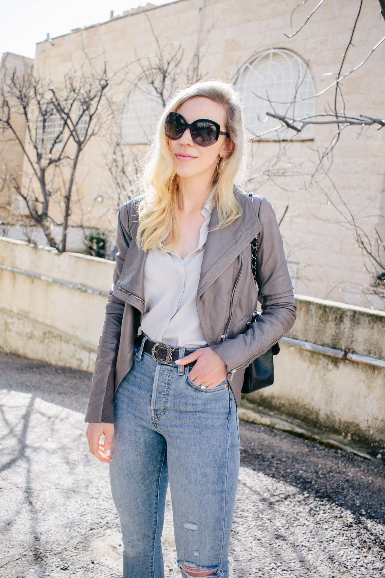Meagan Brandon fashion blogger of Meagan's Moda shares gray leather jacket  outfit idea for spring with light gray blouse, Saint Laurent black leather  belt and Levi's wedgie skinny light blue jeans 