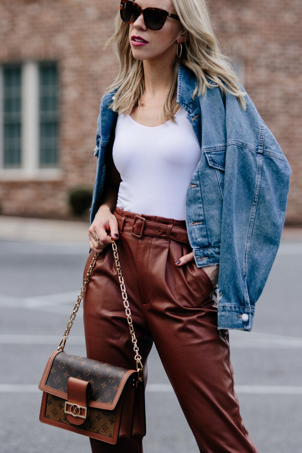 Meagan Brandon fashion blogger of Meagan's Moda wears boxy cropped denim  jacket with white bodysuit, brown faux leather pants and Louis Vuitton Dauphine  bag - Meagan's Moda