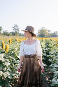 Meagan Brandon fashion blogger of Meagan's Moda wears linen puff sleeve blouse with brown pleated skirt in sunflower field